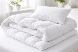 Helle, frisch gewaschene Bettdecke und Kopfkissen ohne Bezug liegen locker gefaltet auf einem Bett und sind bereit zum Waschen.