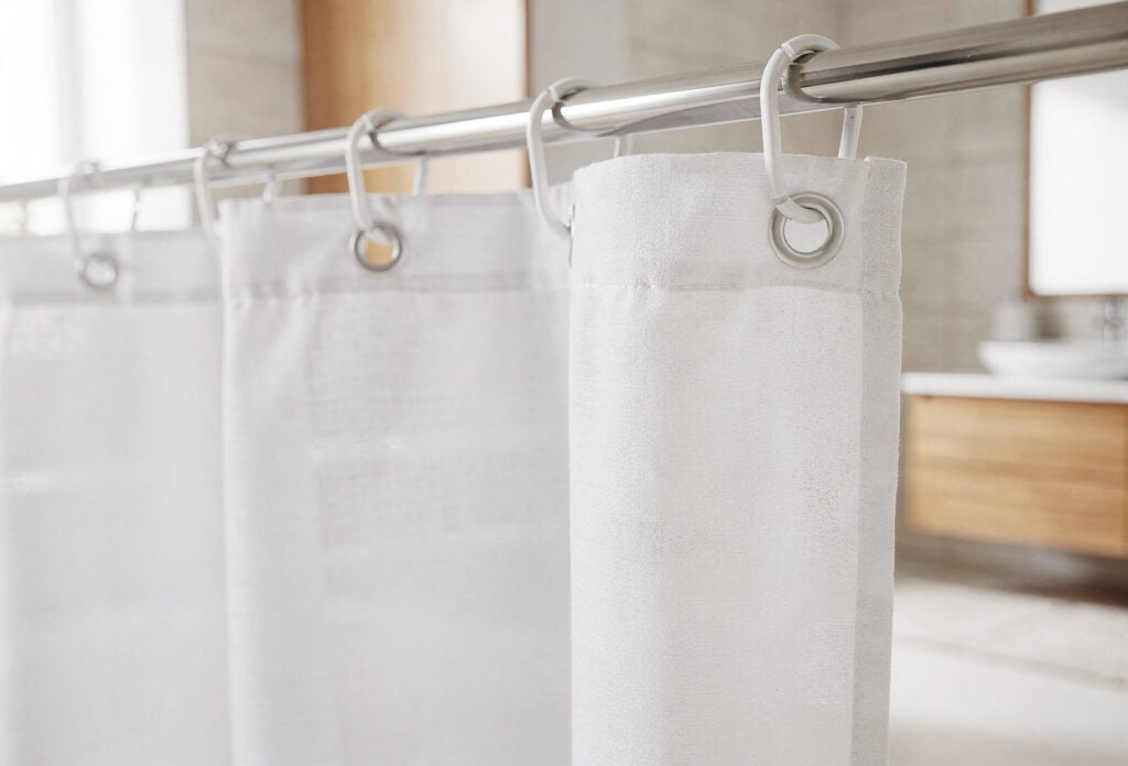 Weißer Duschvorhang mit Kunststoffringen an einer Metallstange in einem hellen Badezimmer – sauber und frisch aufgehängt nach dem Waschen