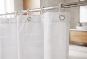 Weißer Duschvorhang mit Kunststoffringen an einer Metallstange in einem hellen Badezimmer – sauber und frisch aufgehängt nach dem Waschen
