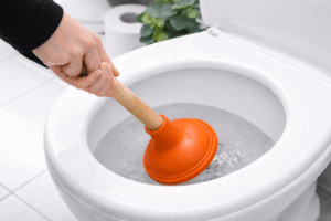 Hand benutzt einen Pömpel in einer weißen Toilette, um eine Verstopfung zu lösen.