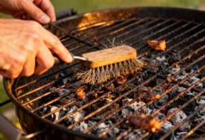Grillrost reinigen: Eingebrannte Essensreste und Fett werden auf einem Holzkohlegrill im Garten entfernt
