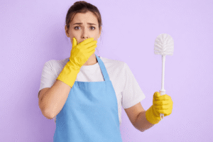 Frau mit gelben Handschuhen und Klobürste in der Hand schaut überrascht – humorvolle Darstellung zum Thema Klobürste wechseln im Badezimmer
